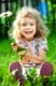 Happy smiling child with flower sitting on green grass outdoors in spring garden